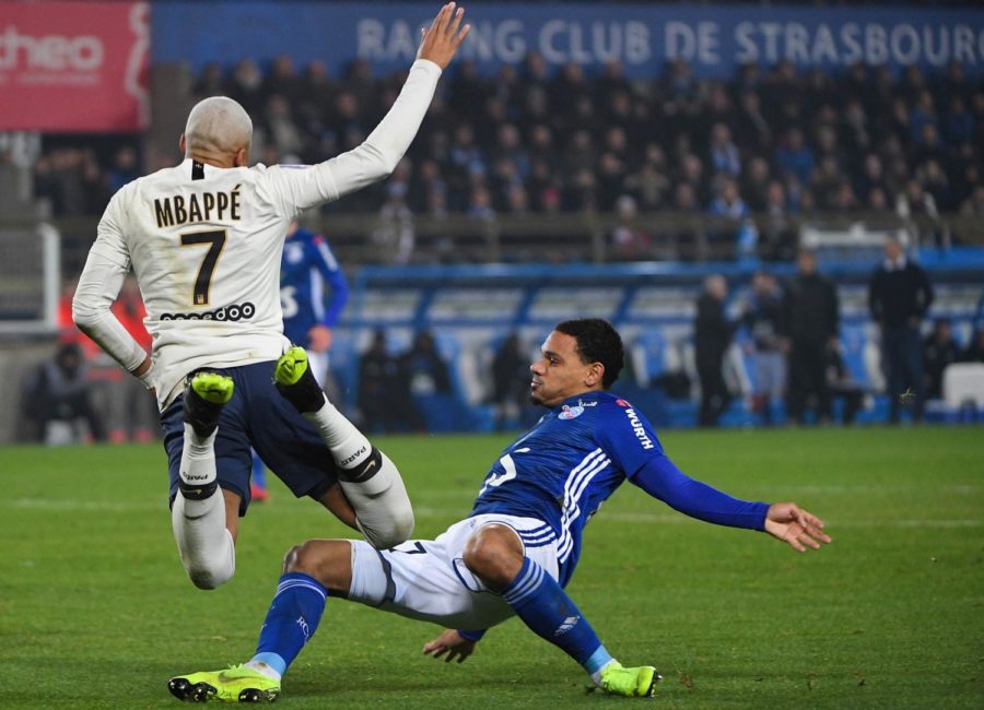 Paris Saint-Germains French forward Kylian Mbappe (L) falls on the football as he vies for the ball with Strasbourgs French defender Kenny Lala (R)