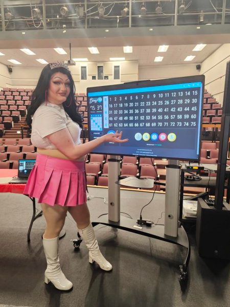 Student Queen Enby  Vivacious posing with the bingo board                                                                                                                                                                                                                                                                                                